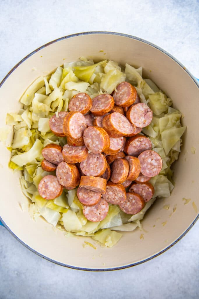 Sliced sausage placed on top of fried cabbage in a dutch oven.
