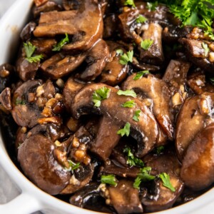 Overhead image of sautéed mushrooms in a white bowl with parsley on top.