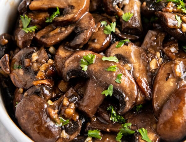 Overhead image of sautéed mushrooms in a white bowl with parsley on top.
