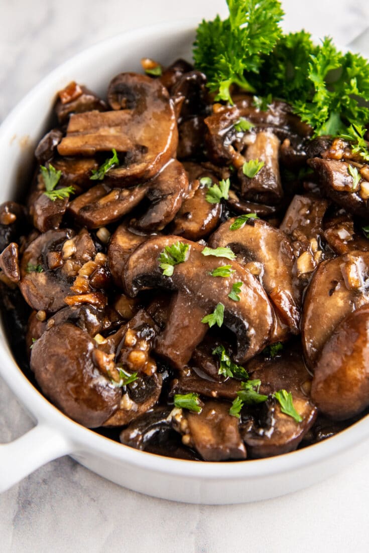 Overhead image of sautéed mushrooms in a white bowl with parsley on top.