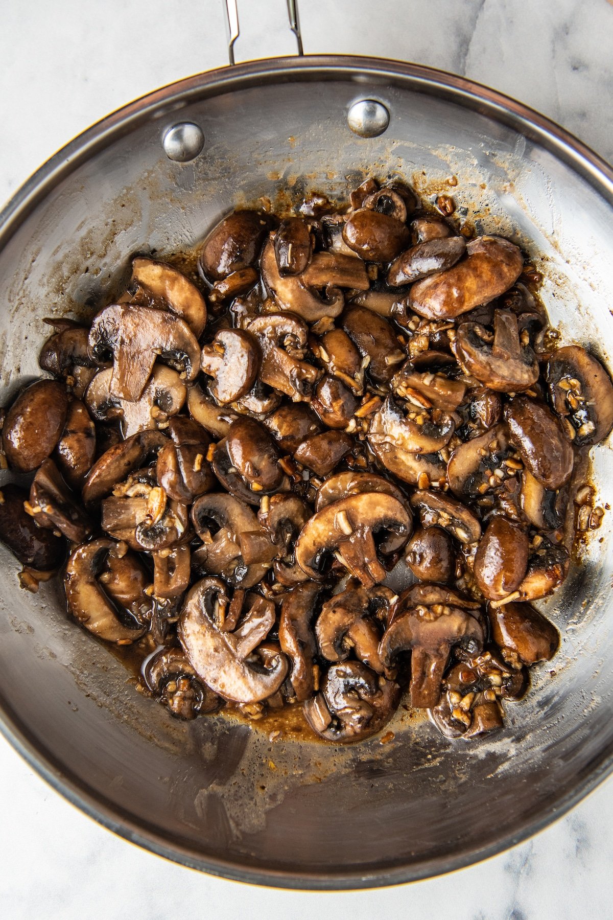 French onion sautéed mushrooms in a silver skillet with a wooden spoon.