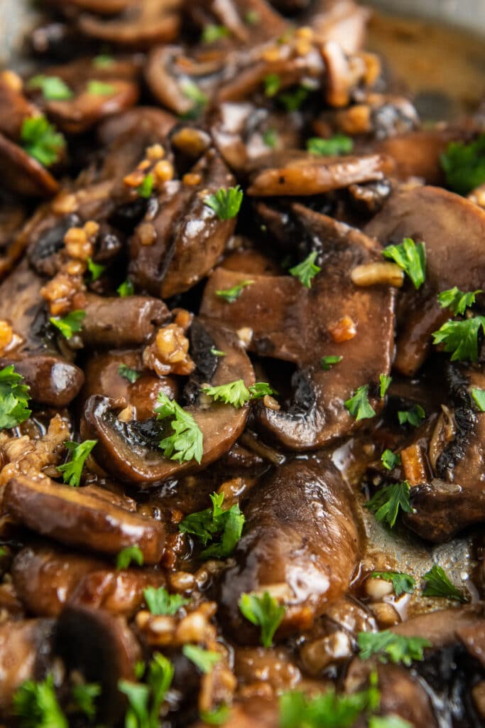 Sautéed mushrooms sprinkled with parsley in a skillet.
