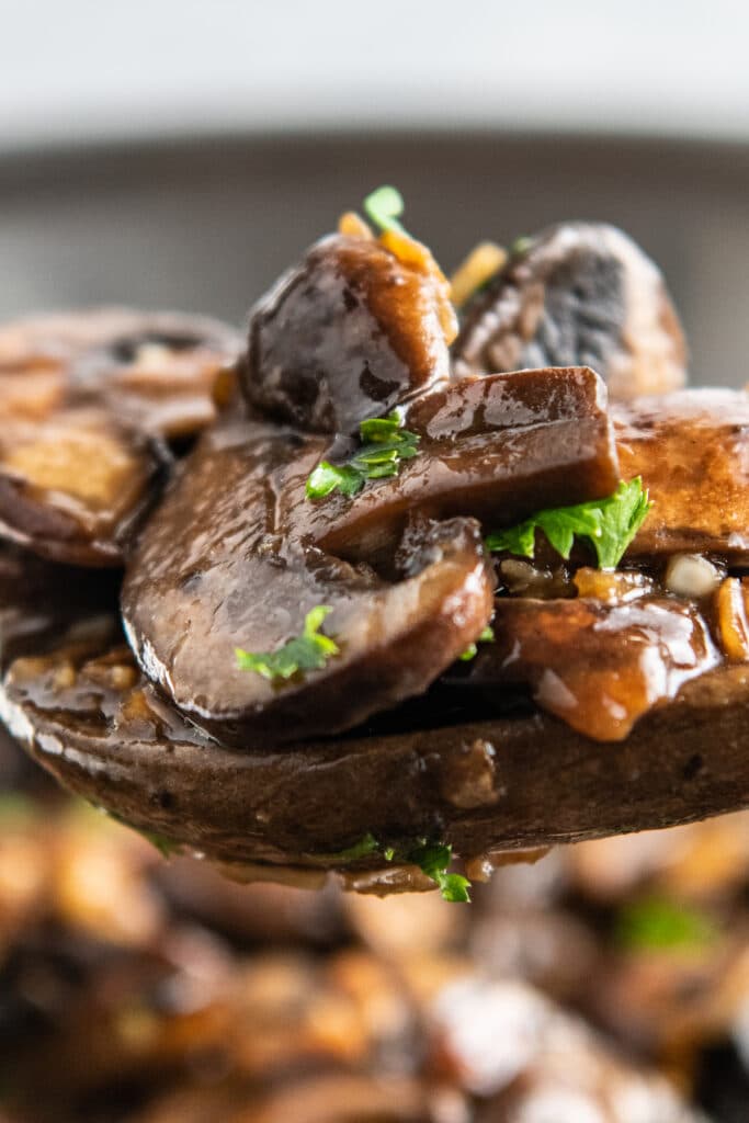 An up close image of sautéed mushrooms on a wooden spoon with parsley.