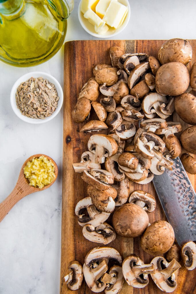 Sliced mushrooms on a wooden cutting board with a knife.