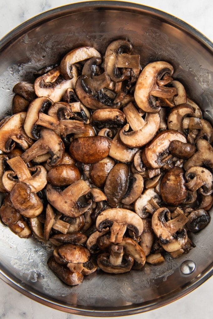 Mushrooms that are being sautéed in a metal skillet.