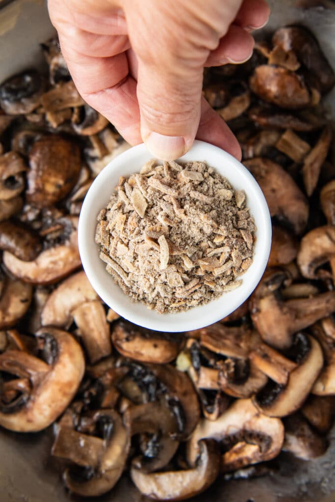 A white bowl with seasonings in it over a skillet with sliced mushrooms.