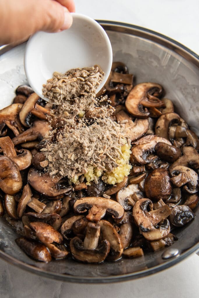French onion soup mix being poured into a skillet filled with sautéed mushrooms.
