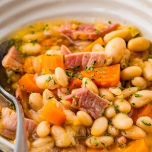 Up close image of ham and beans in a white bowl with a spoon.