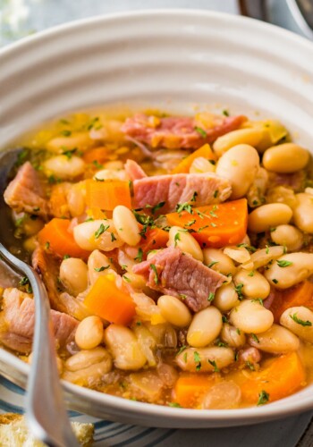 Up close image of ham and beans in a white bowl with a spoon.
