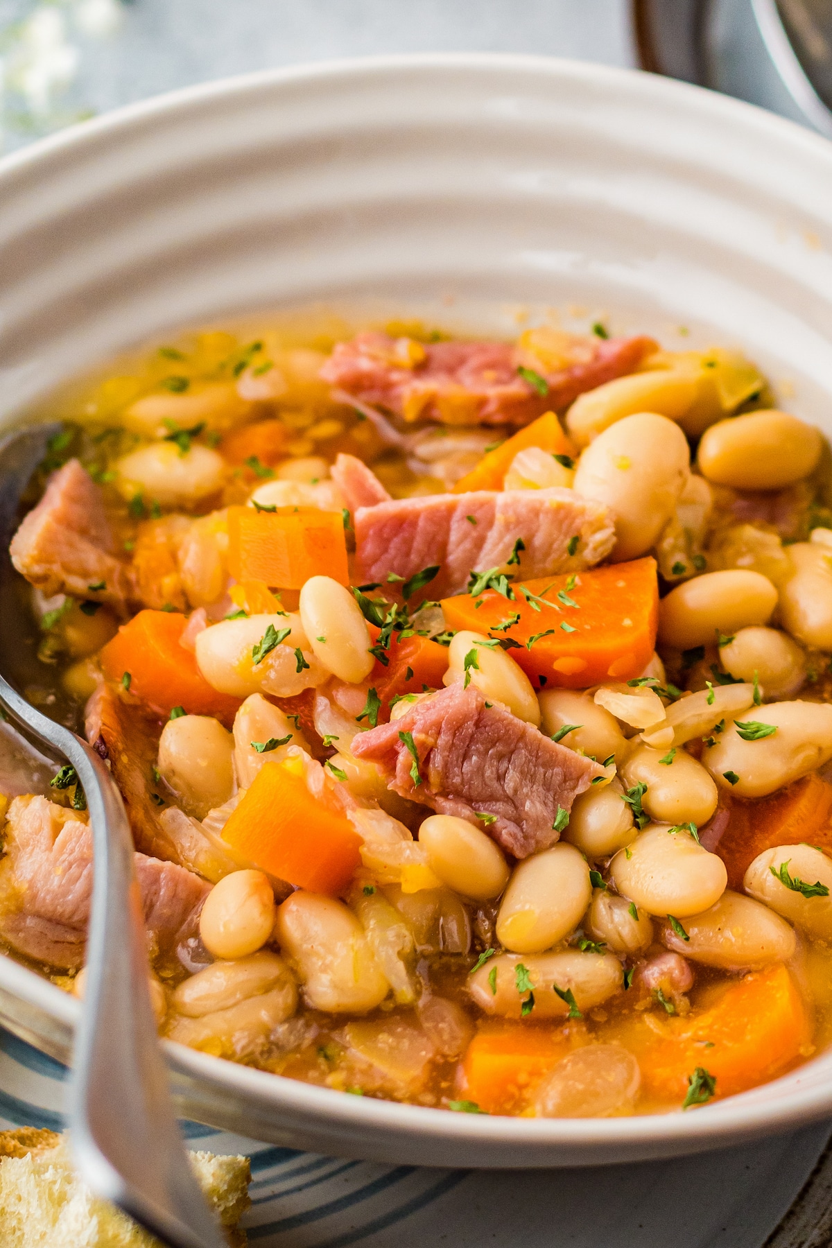 Up close image of ham and beans in a white bowl with a spoon.