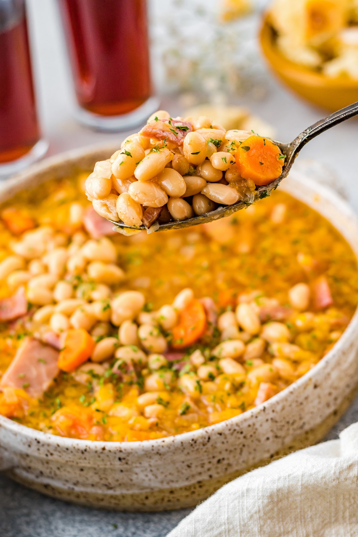 A spoonful of crockpot beans and ham being lifted out of a big bowl.