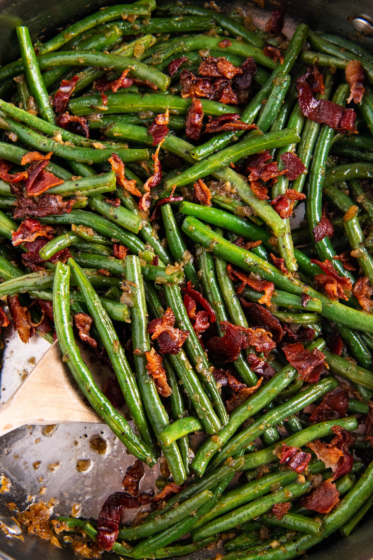 Green beans with bacon in a skillet with a wooden spoon.