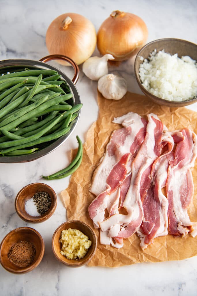 Ingredients for green beans with bacon in bowls and on parchment paper.