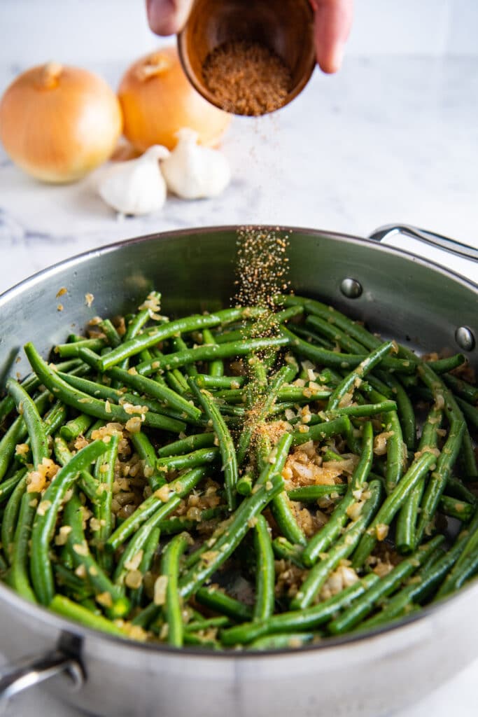 Seasoning being added to a skillet with green beans.
