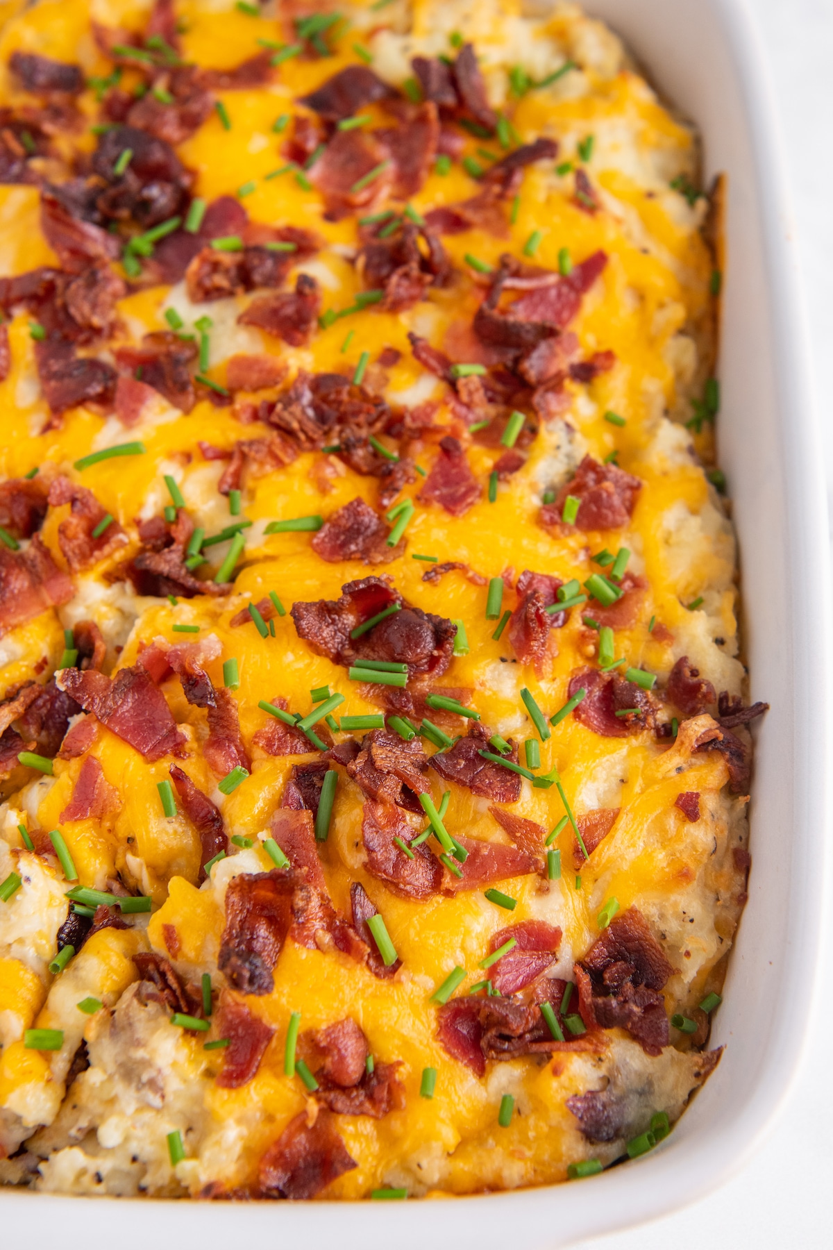 Twice baked potato casserole in a white casserole dish with chives on top.