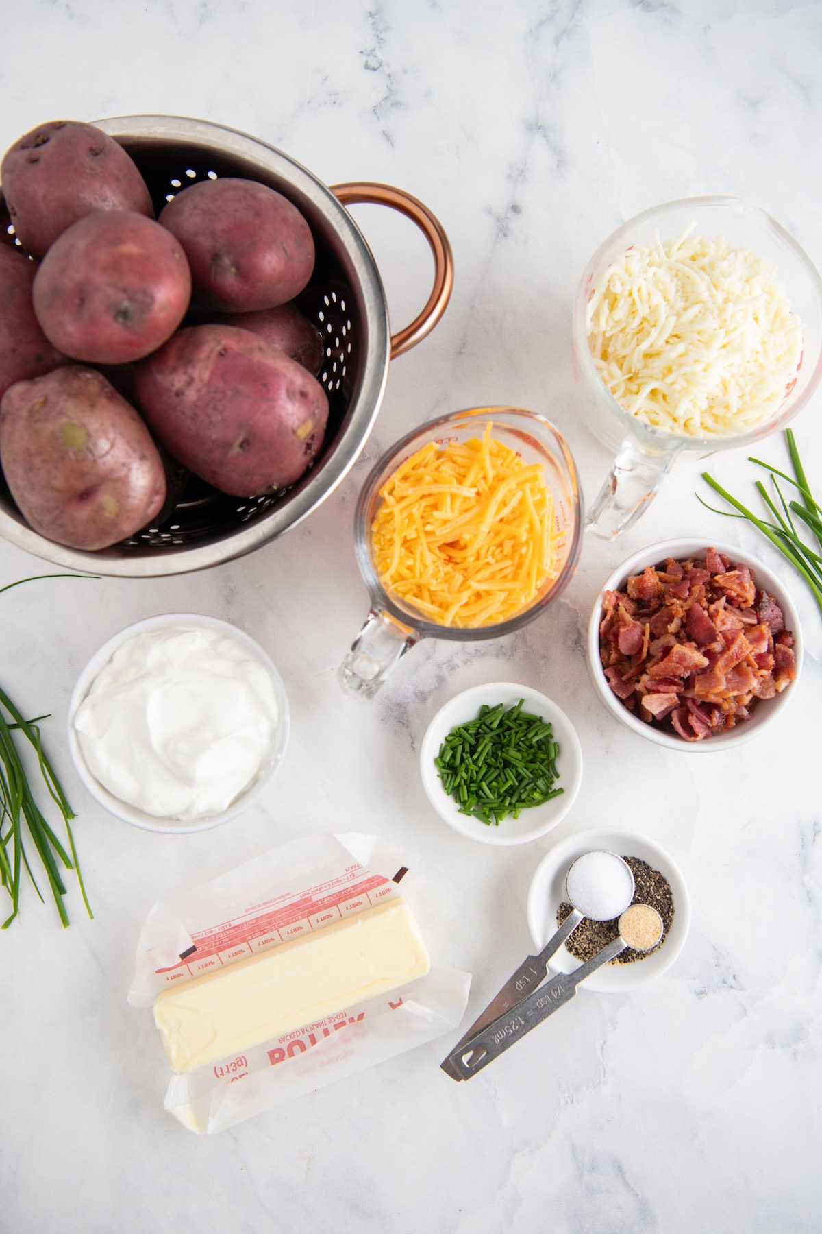 Ingredients for twice baked potato casserole in bowls on a marble background.