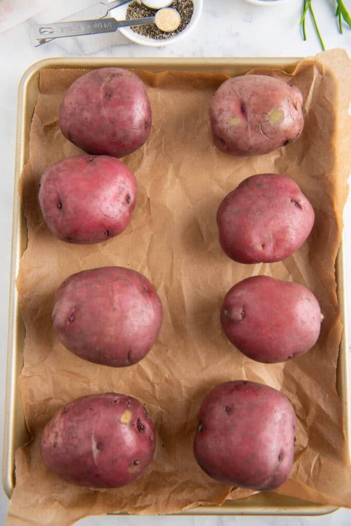 Red potatoes placed on brown parchment paper on a metal cookie sheet.
