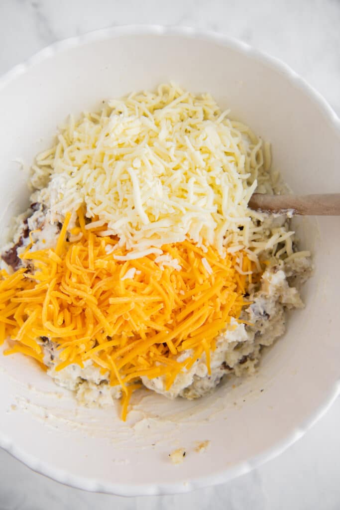 A bowl with mashed potatoes with two types of shredded cheese on top.