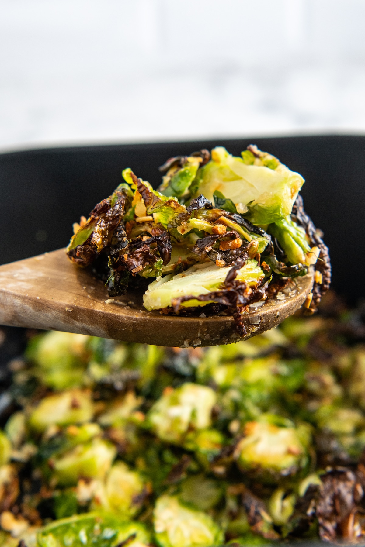 Brussels sprouts being scooped out of an air fryer with a wooden spoon.