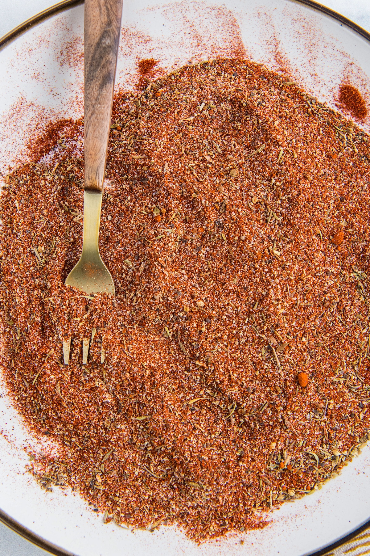 Homemade cajun seasoning spread out on a white plate with a fork after mixing.