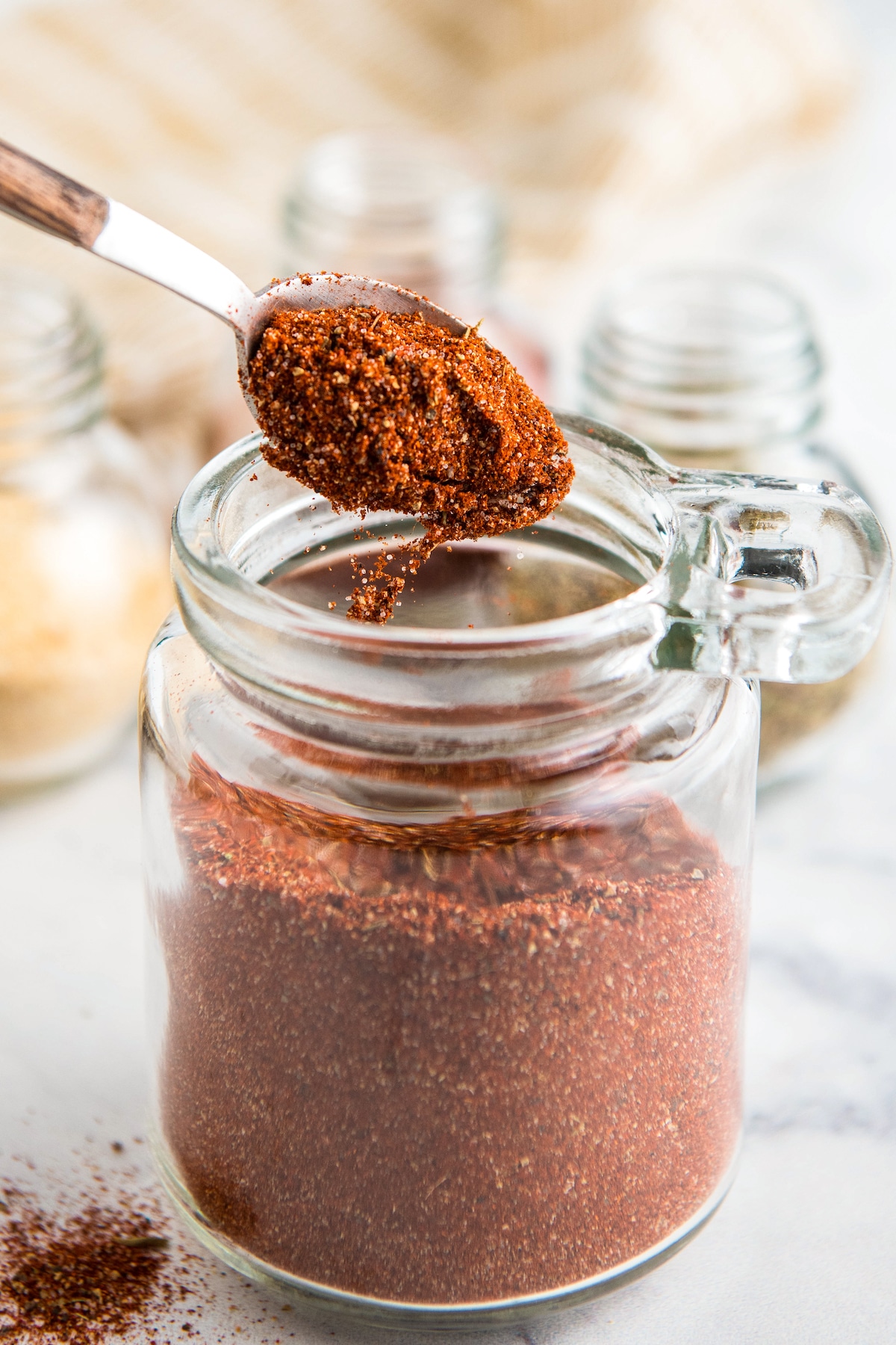 Cajun seasoning being poured off a spoon into a glass jar.