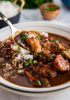 A spoonful of chicken and sausage gumbo being scooped up from a bowl.