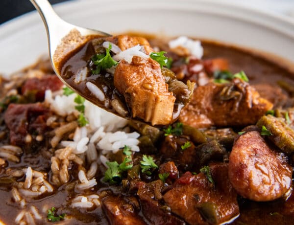 A spoonful of chicken and sausage gumbo being scooped up from a bowl.