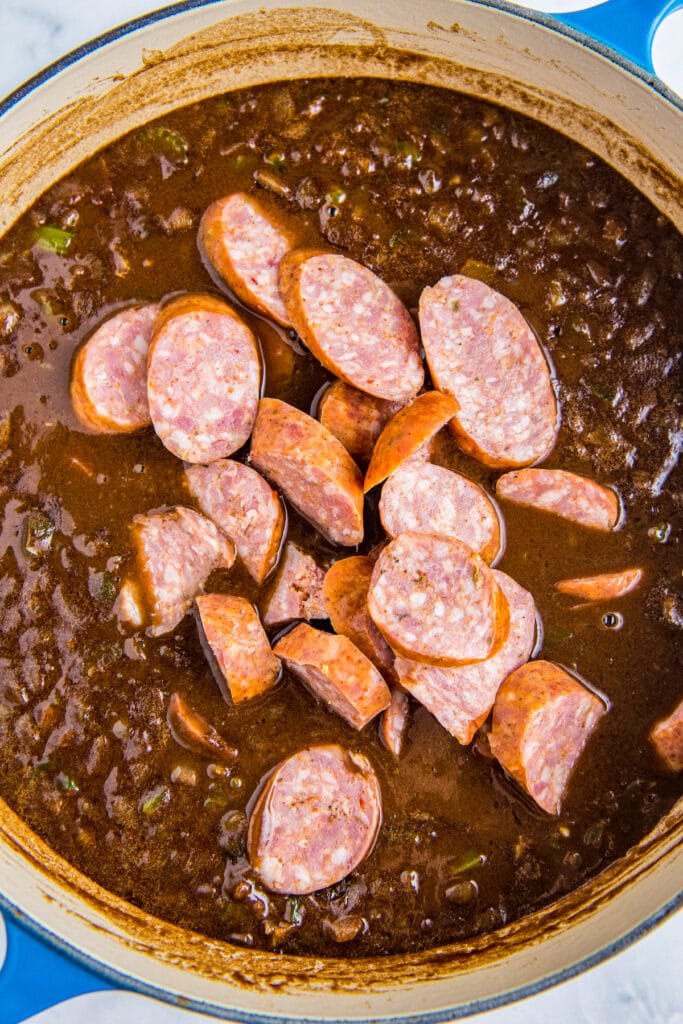 Sausage being added to gumbo in a pot.