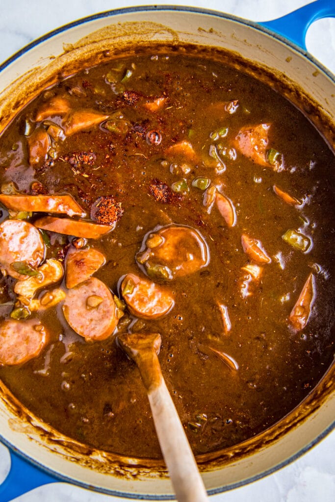 Stirring seasonings into a pot of gumbo with a wooden spoon.