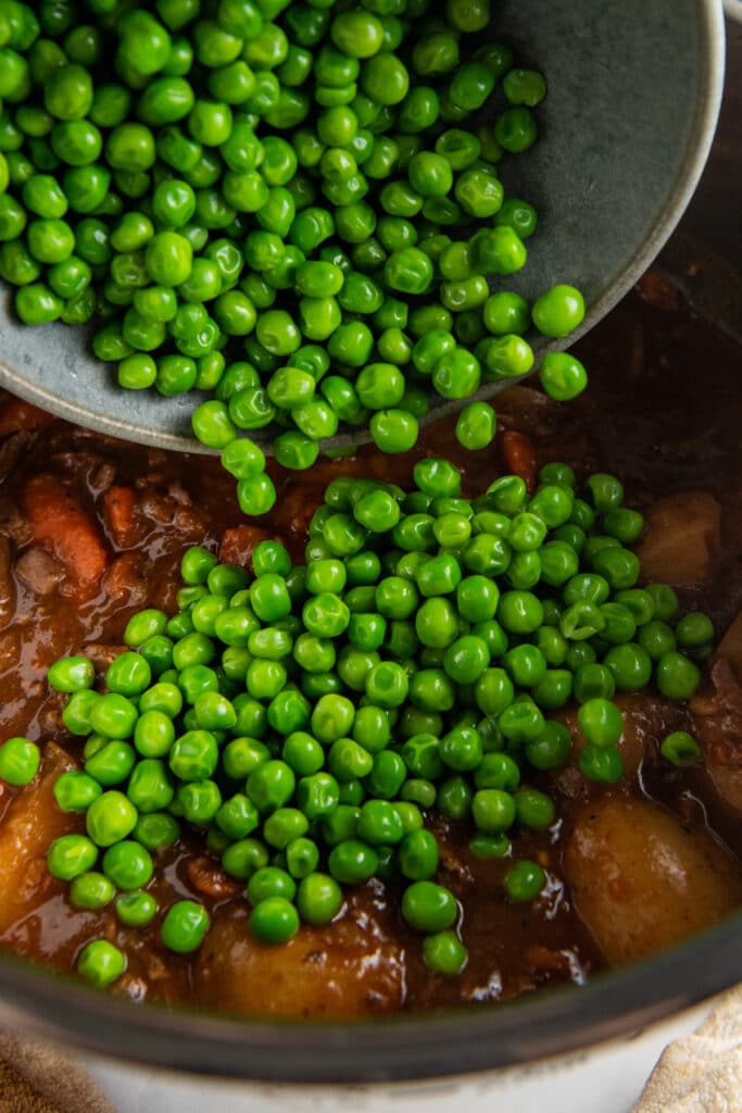 Peas being poured into an instant pot filled with beef in broth.