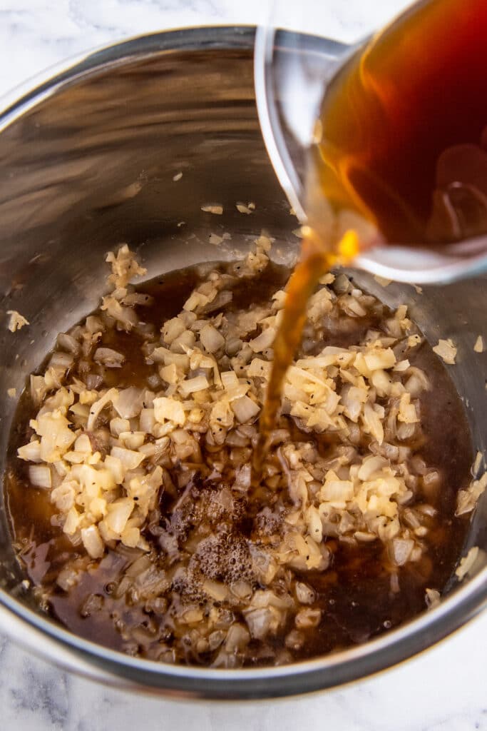 Beef broth being poured into an instant pot with onions.