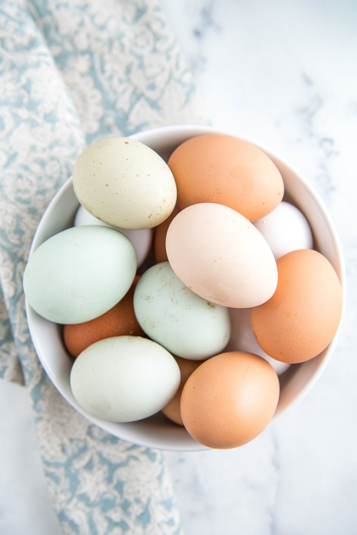 Colorful eggs in a white bowl with a tea towel.