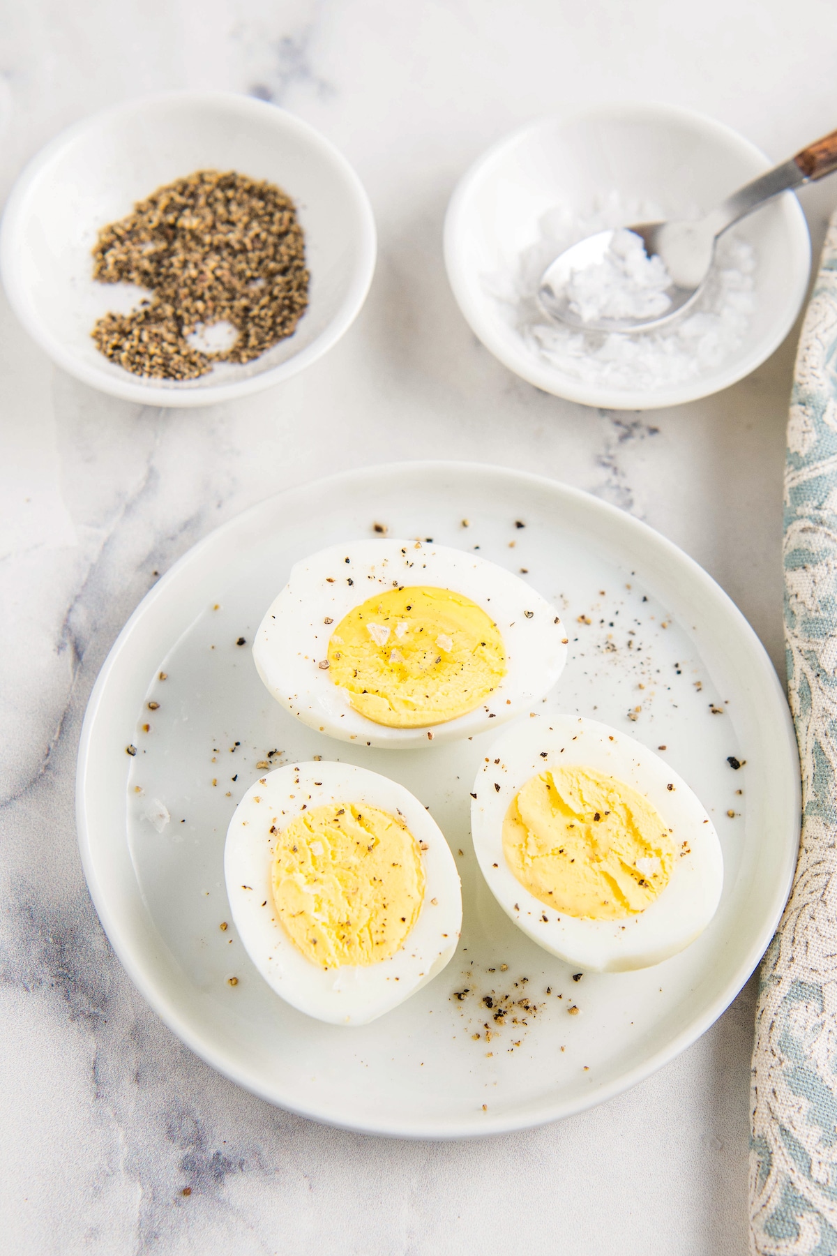 Air fryer hard boiled eggs on a white plate with salt and pepper on them.