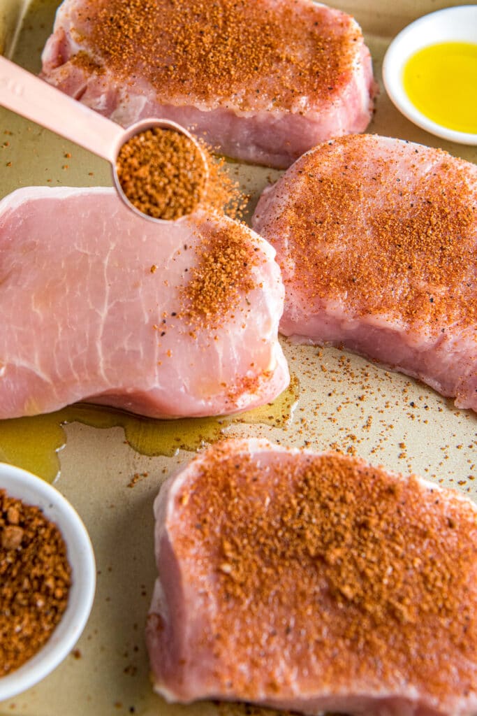 Raw pork chops being sprinkled with seasoning.