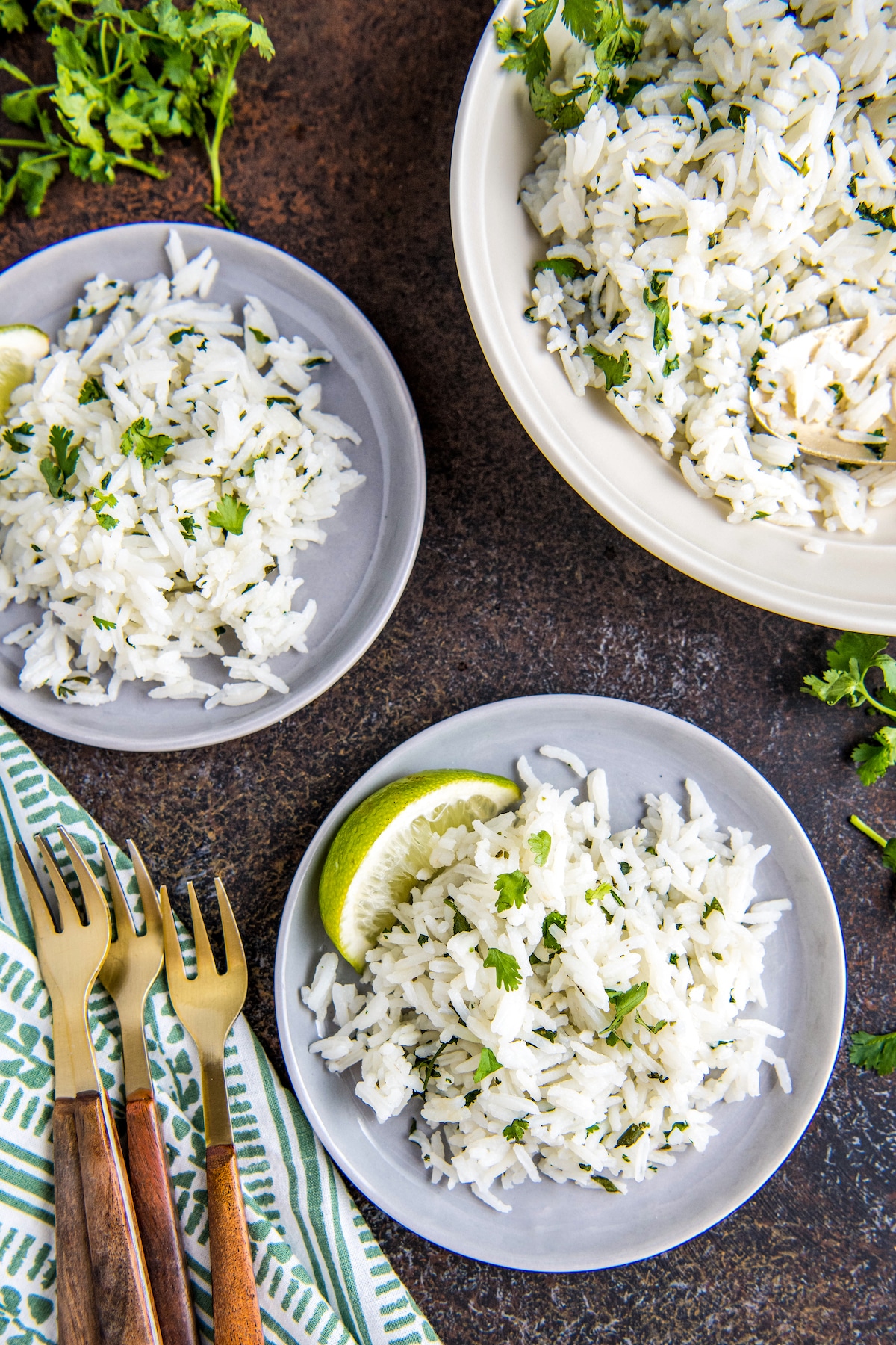 Three bowls of rice with cilantro and lime wedges and four forks on a napkin.