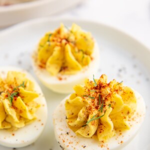 Three southern deviled eggs on a white plate with smoked paprika, chives and pepper on top.