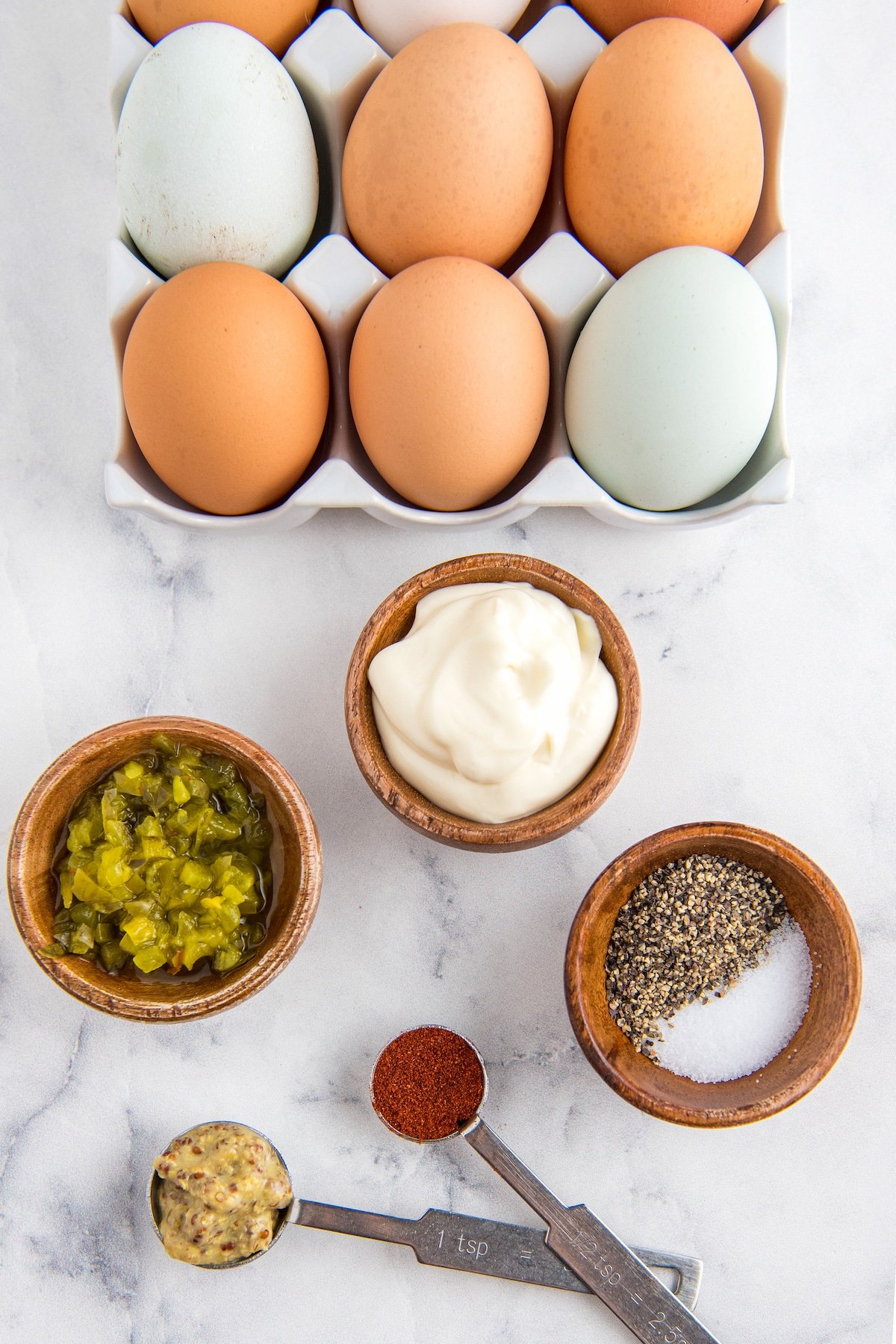 Eggs in an egg carton and other ingredients arranged in wooden bowls.