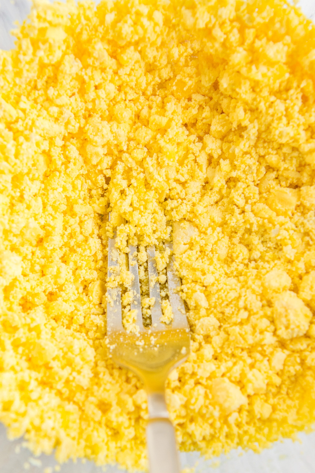 Mashed egg yolks in a bowl with a fork.