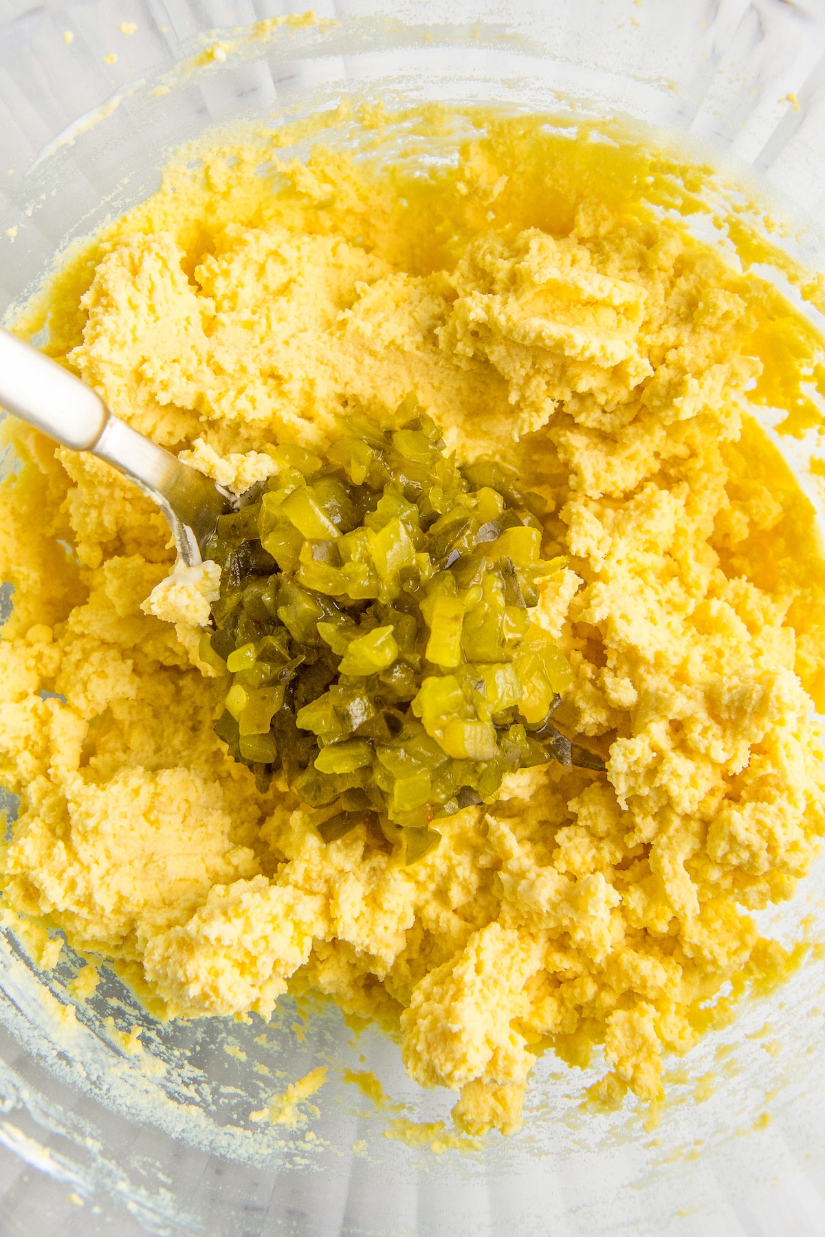 Relish being added to a bowl of mashed egg yolks.