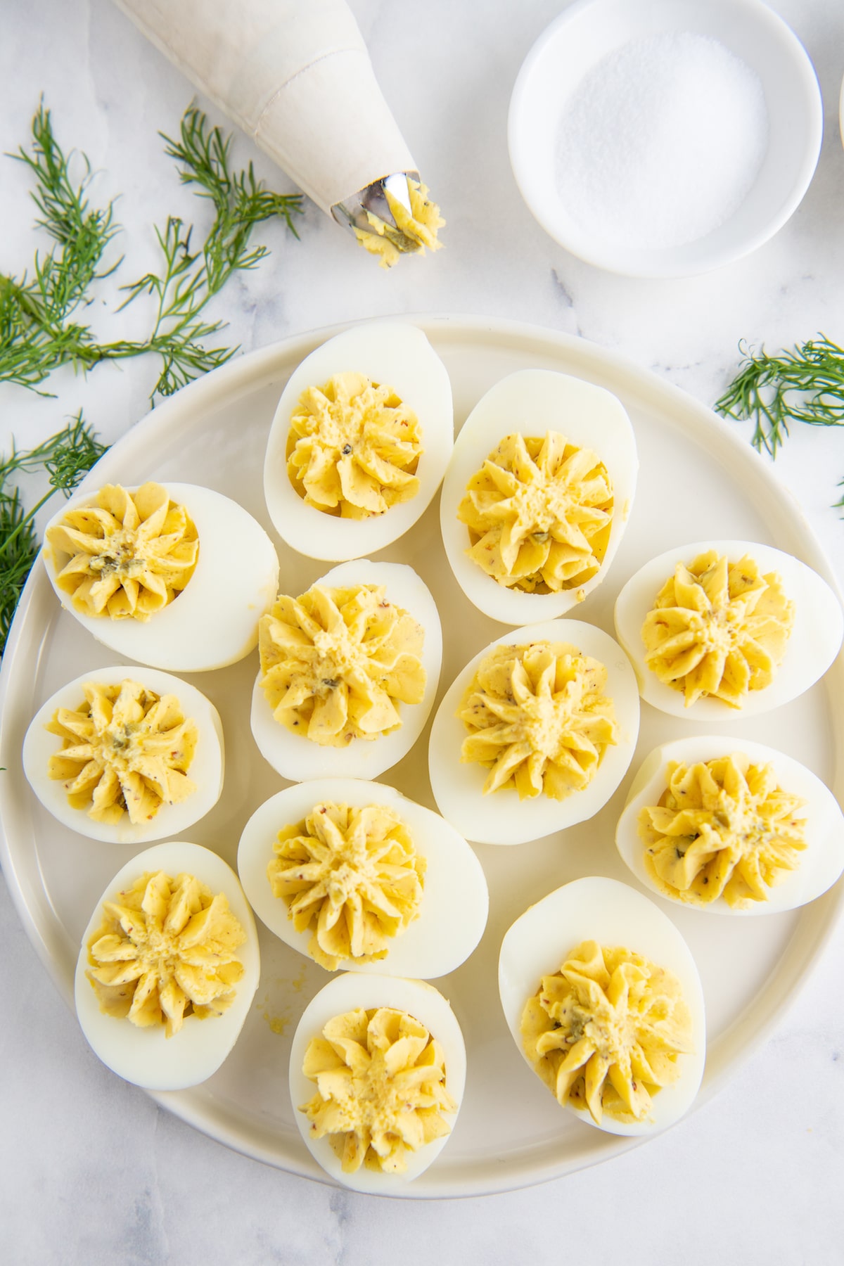 Deviled eggs being filled with deviled egg filling on a white plate.