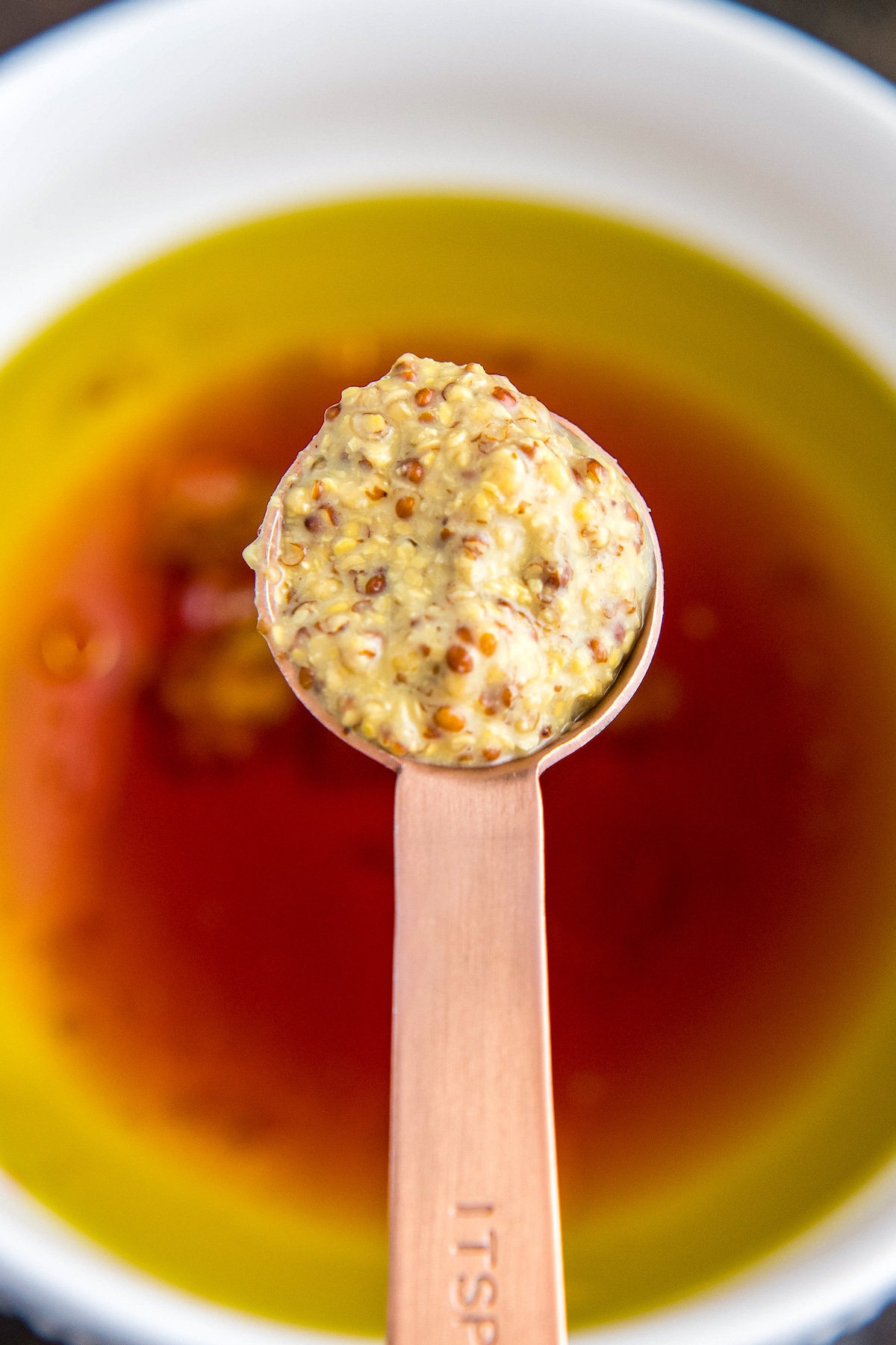A spoonful of Dijon Mustard being added to a bowl.