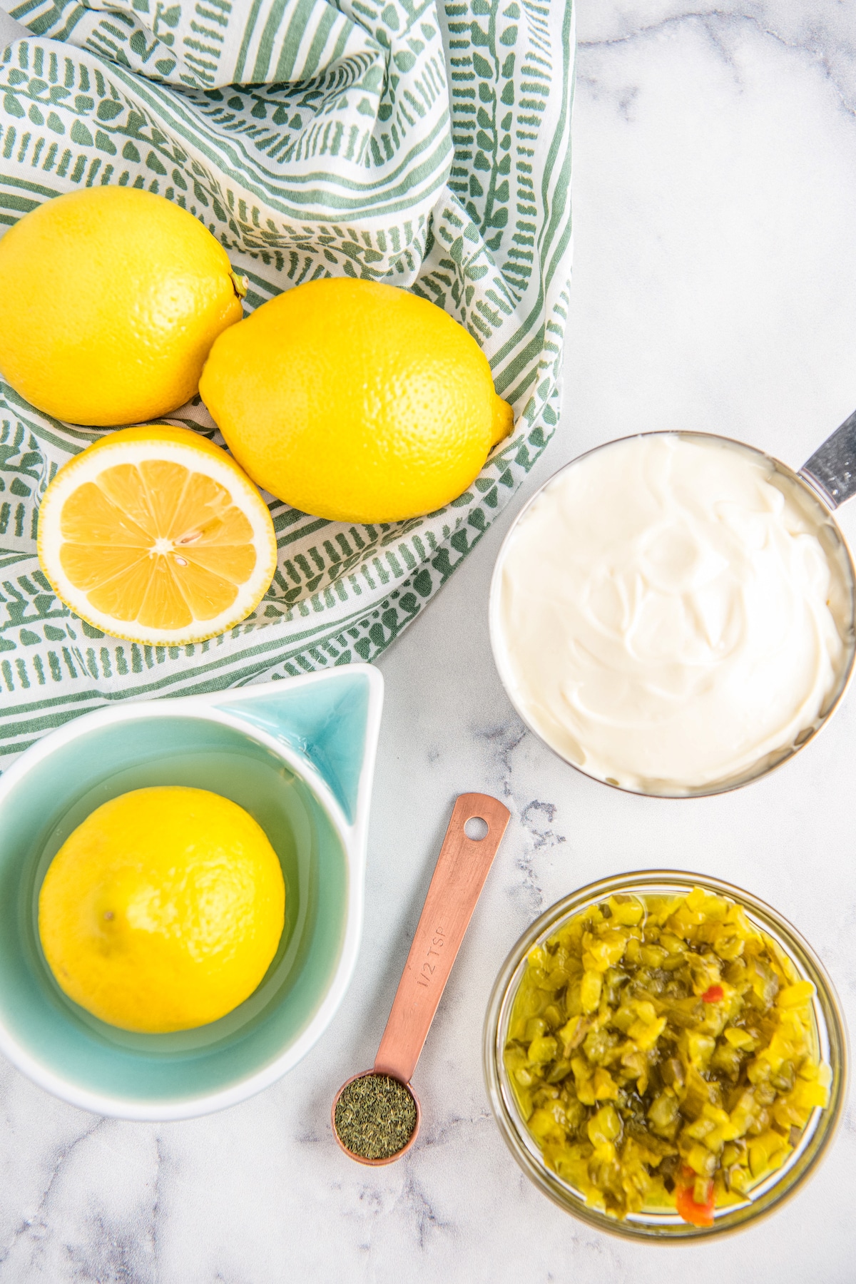 Ingredients for homemade sauce in bowls arranged on a marble countertop.