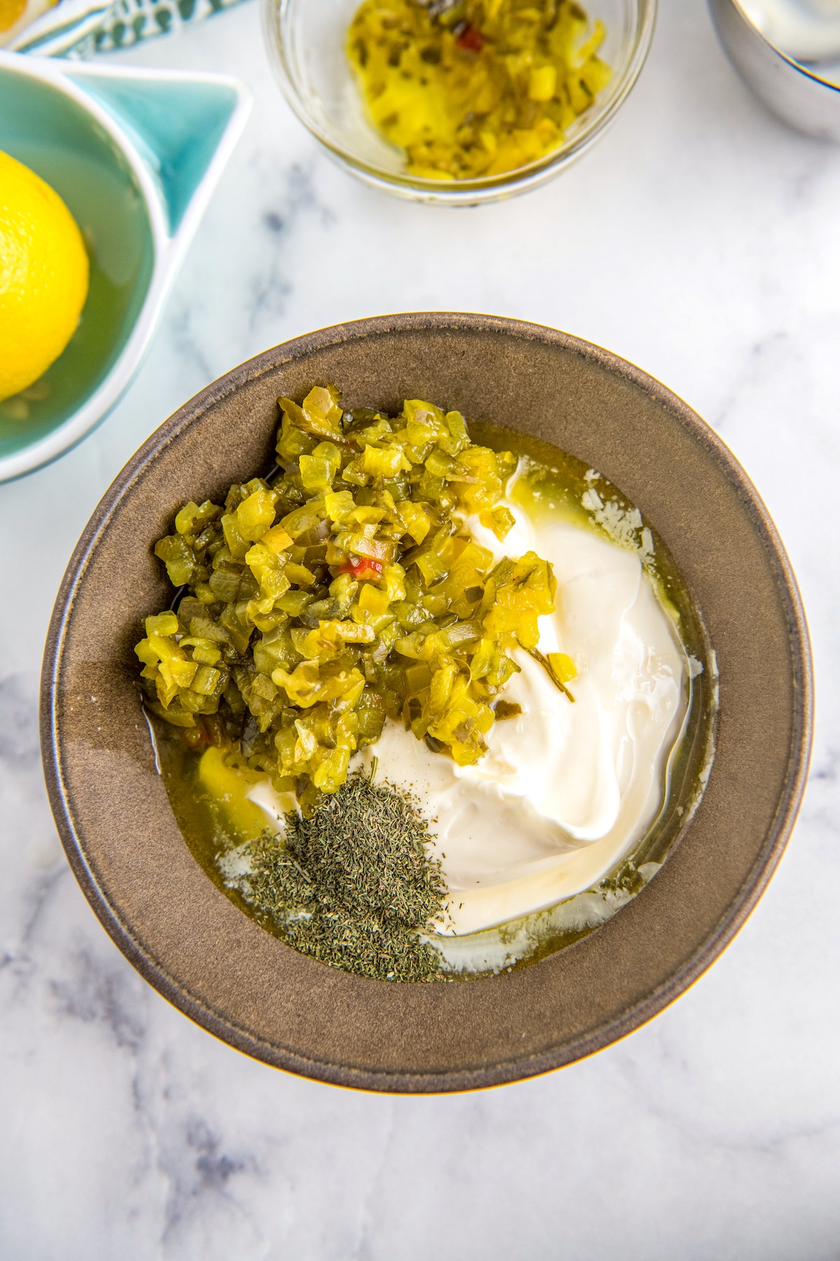 A brown bowl filled with relish, mayo and dried dill.