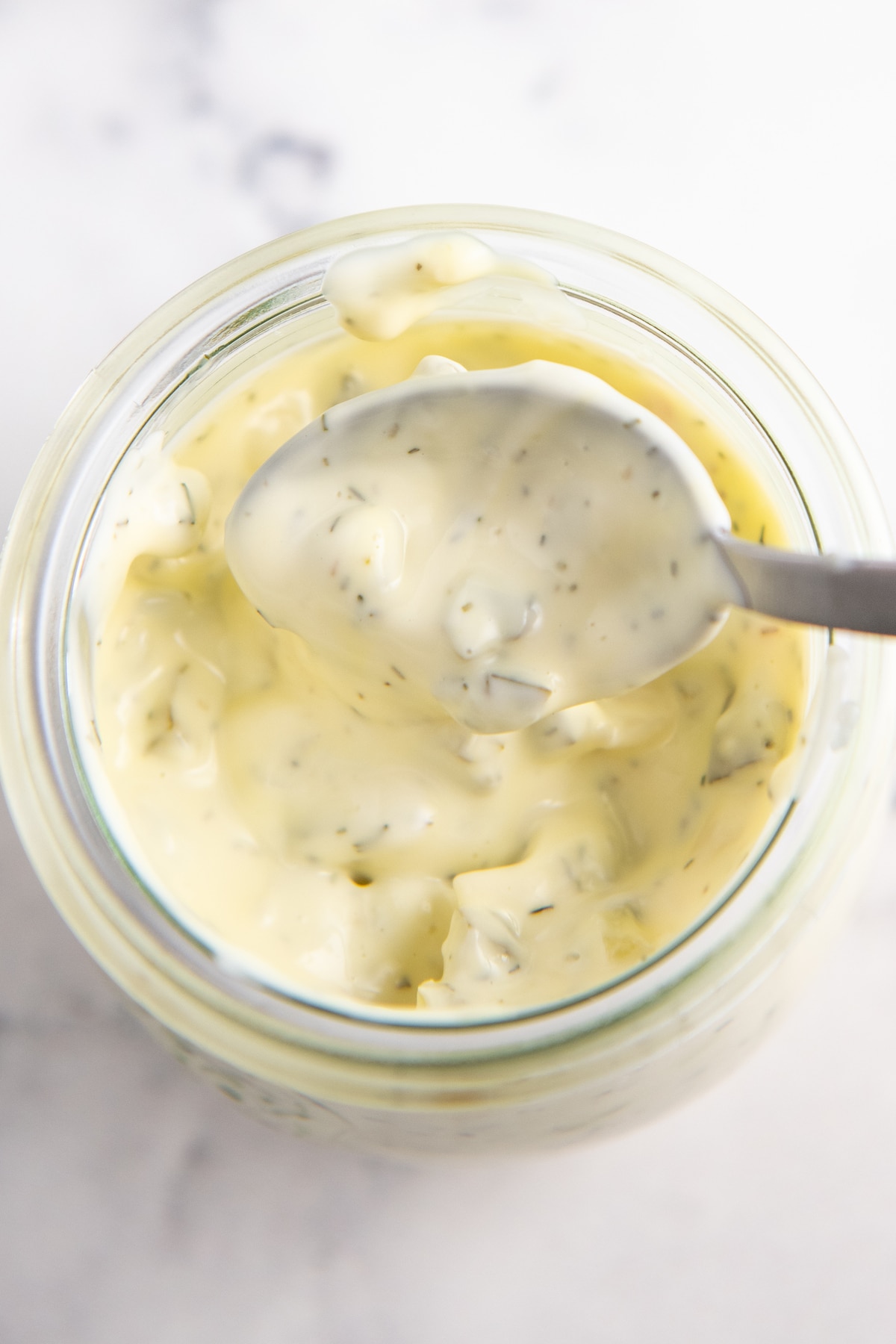 Tartar sauce being scooped out of a jar with a spoon.