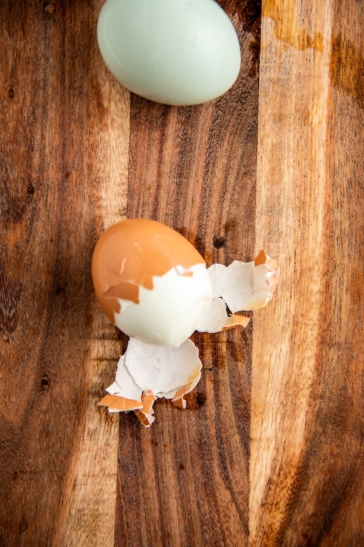 A hard boiled egg being peeled on a cutting board.