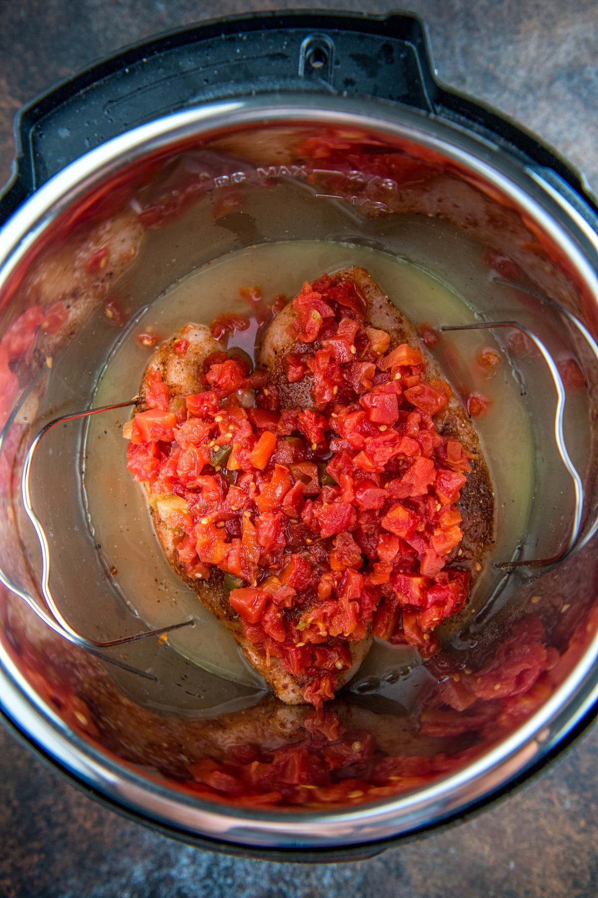 Two uncooked chicken breasts with rotel on top in an instant pot.