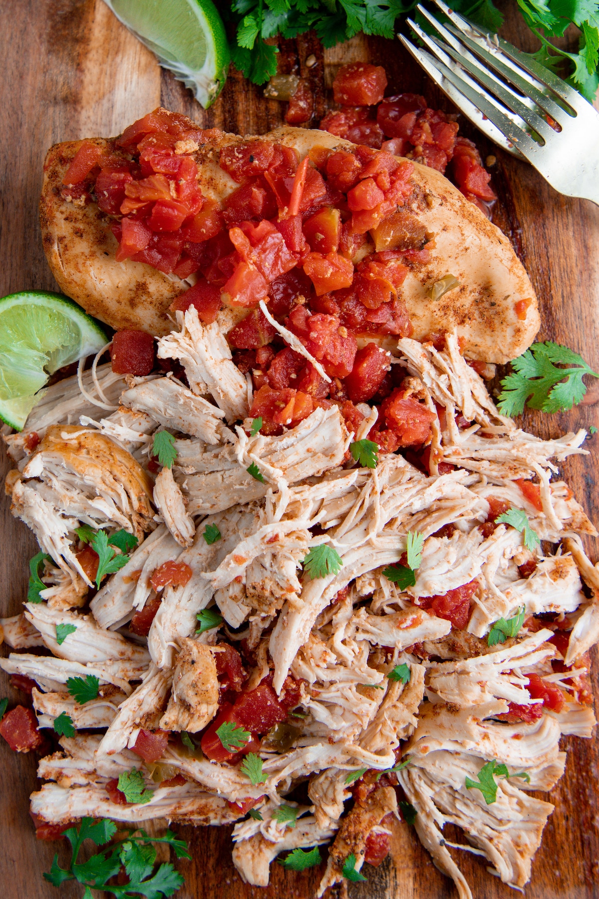 One whole salsa chicken breast and a shredded chicken breast on a cutting board with cilantro on top.