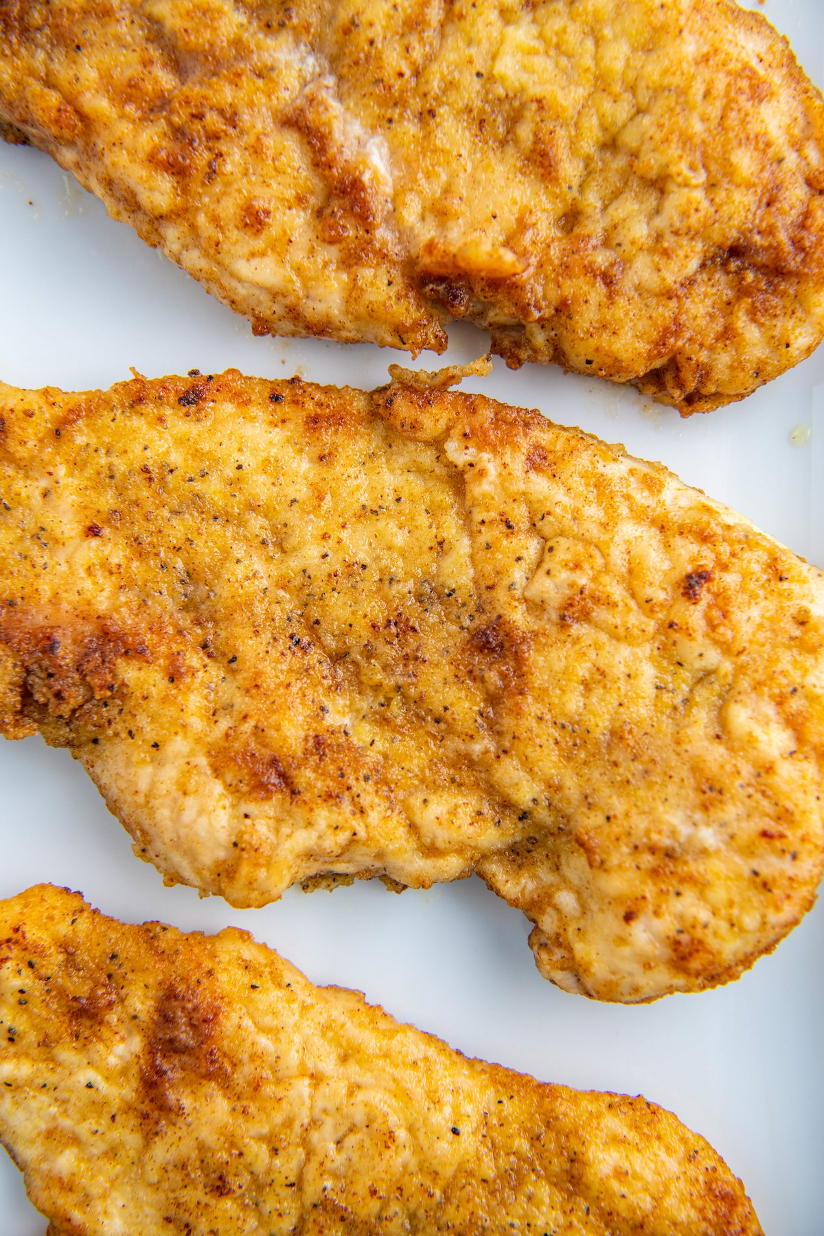 Pan fried chicken breasts on a white plate.