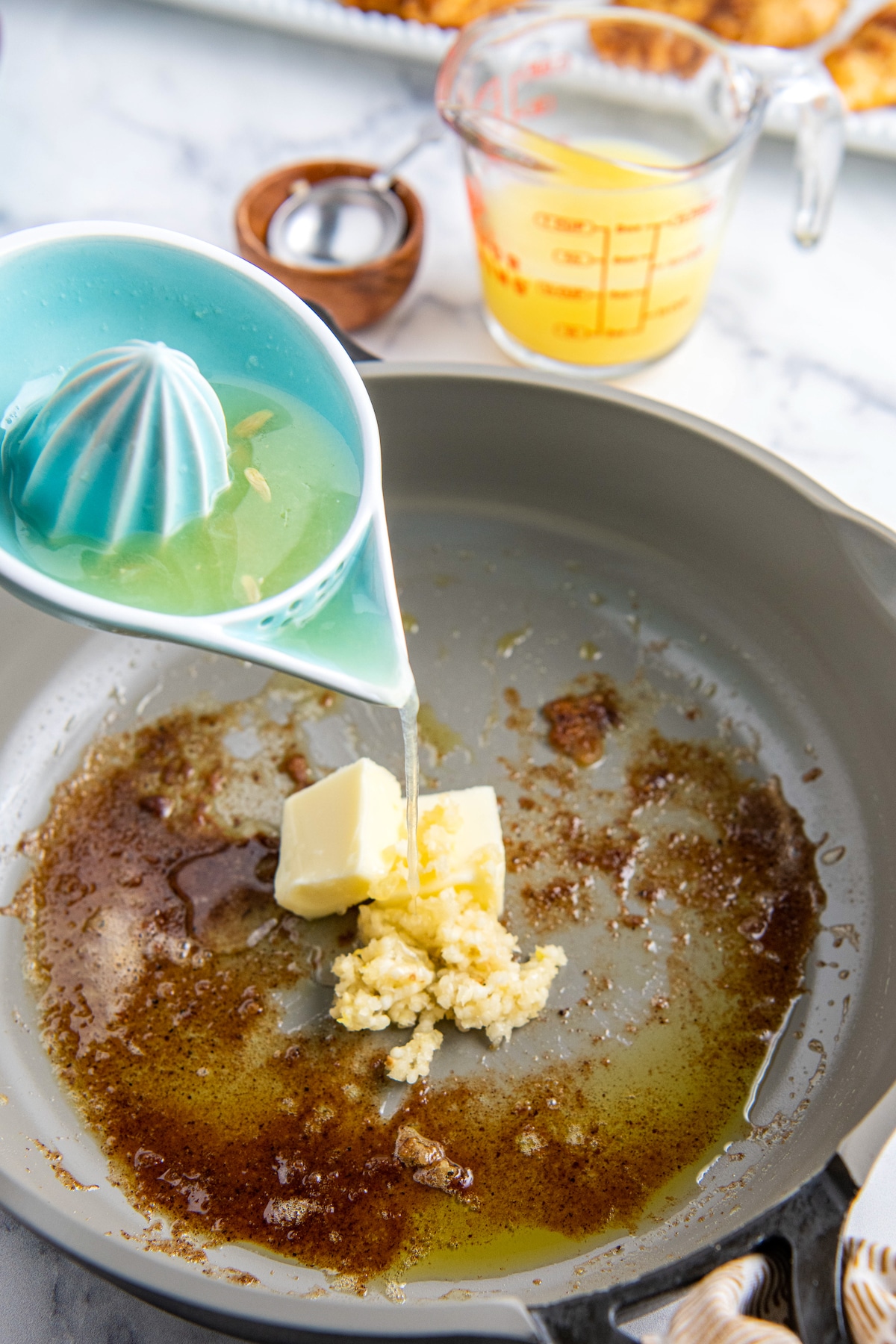 Butter, garlic in a skillet with lemon juice being poured on top.