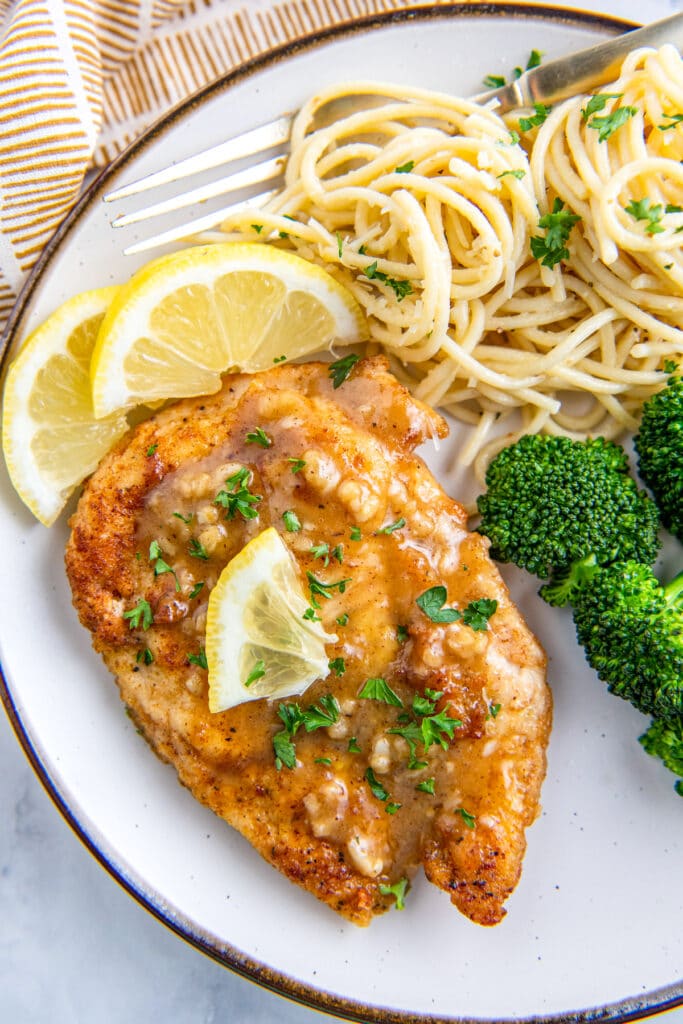 Lemon chicken on a white plate with broccoli and noodles.